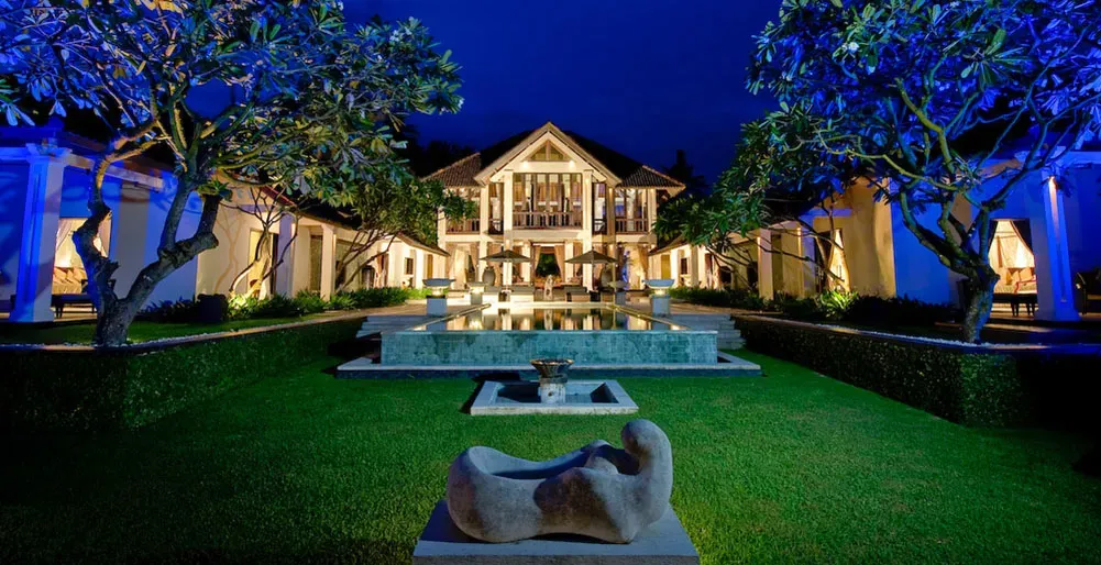 Villa and reflecting pool lit at dusk across an open lawn